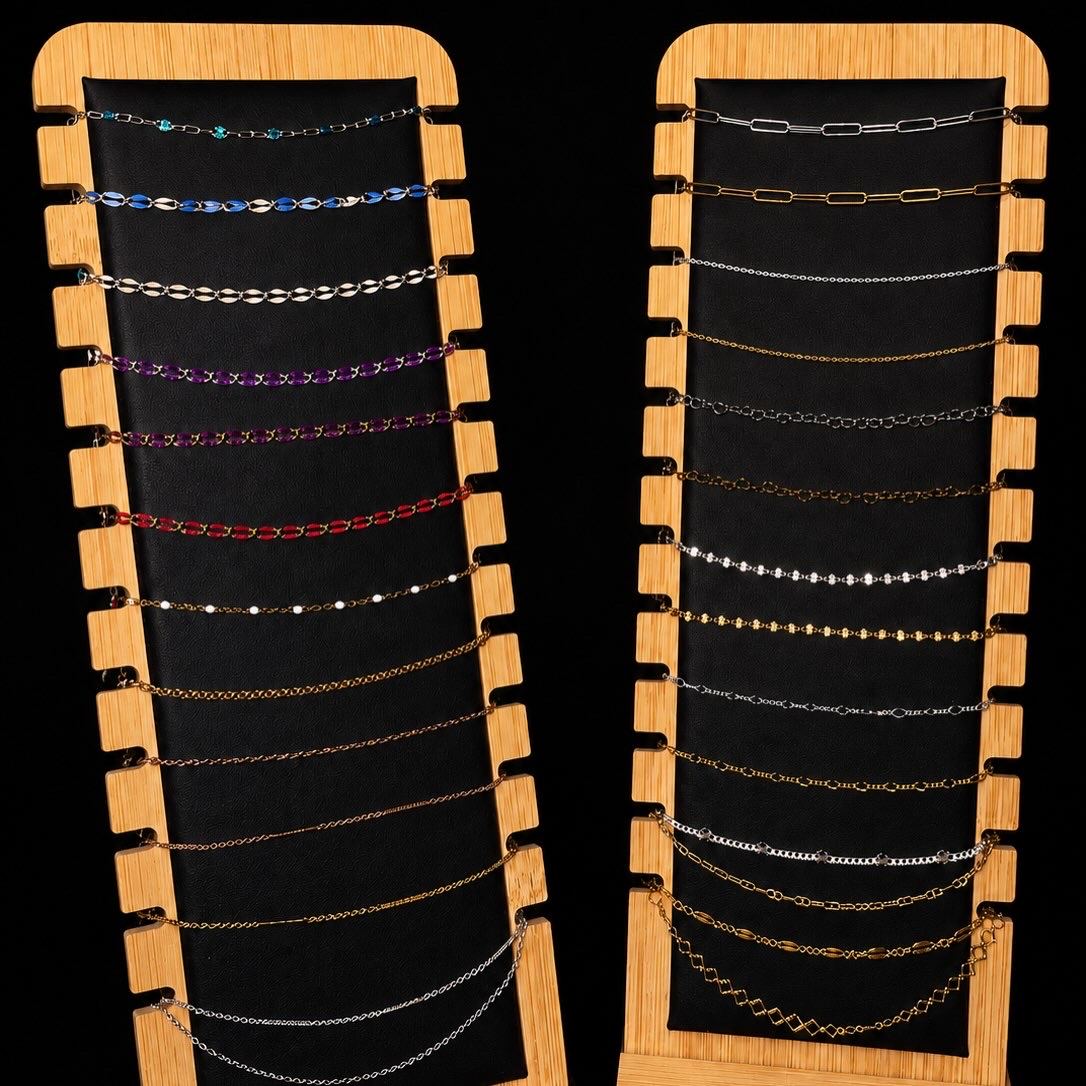 Two wooden display stands holding rows of permanent jewelry chains in gold, silver, and colored enamel.