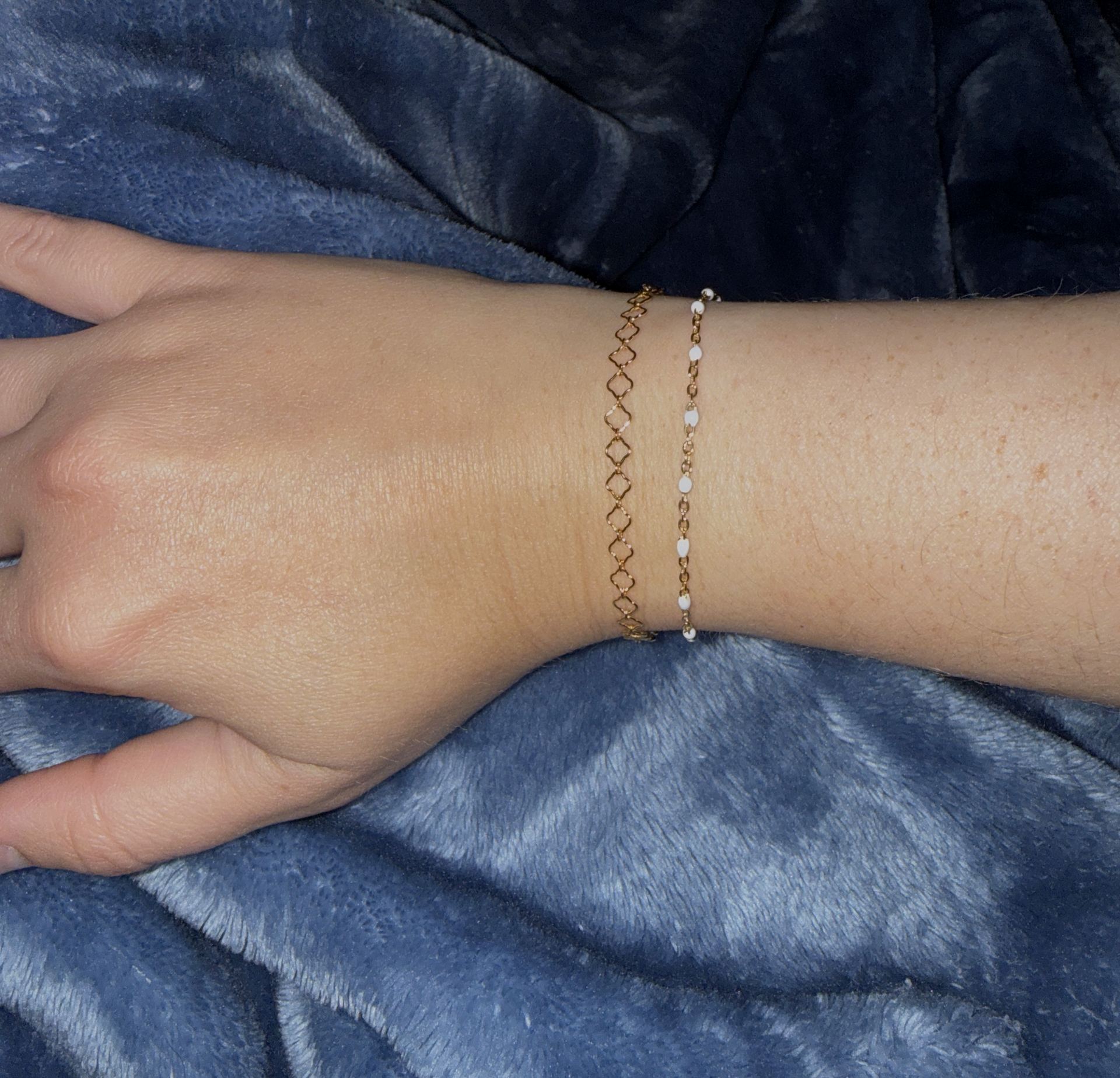 A gold open-link permanent bracelet and a gold chain with white enamel beads worn together on a wrist.