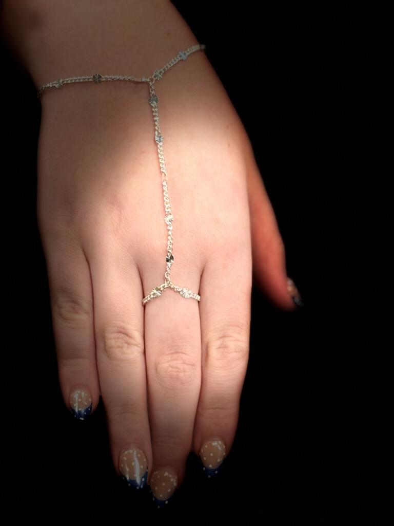 Top view of a silver hand chain, a bracelet at the wrist joined by a single chain to a chain ring on the middle finger.